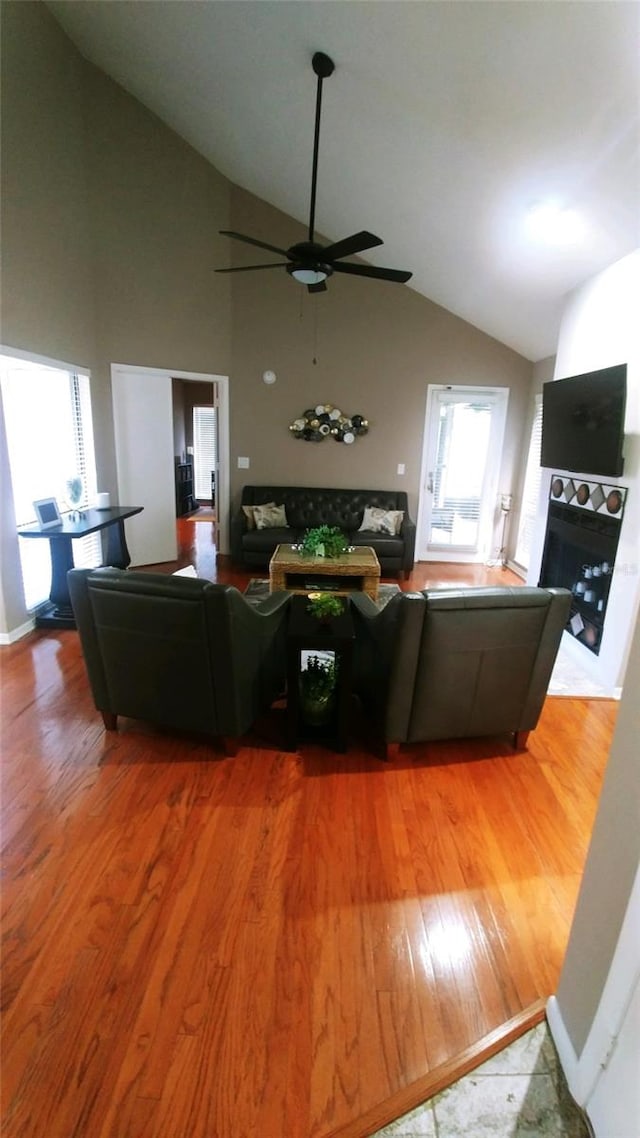 living area with ceiling fan, a fireplace, high vaulted ceiling, and wood finished floors