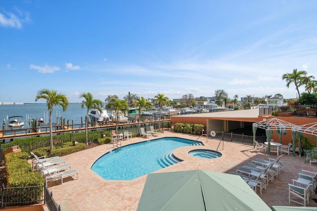 community pool with a water view, a hot tub, fence, and a patio