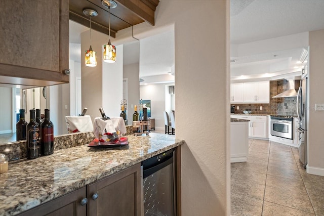 kitchen with beverage cooler, wall chimney exhaust hood, light stone countertops, stainless steel appliances, and white cabinetry