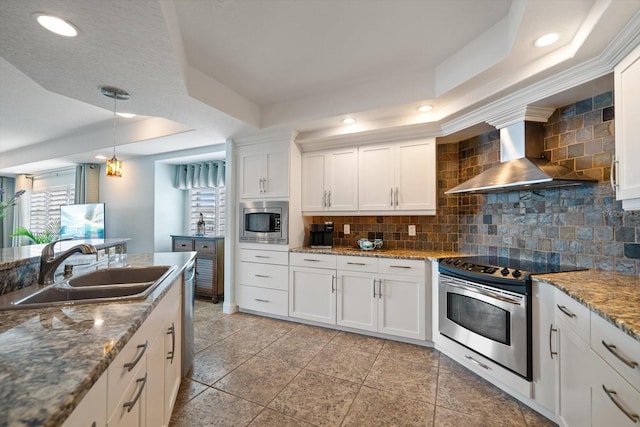 kitchen with stainless steel appliances, a raised ceiling, white cabinets, and wall chimney exhaust hood