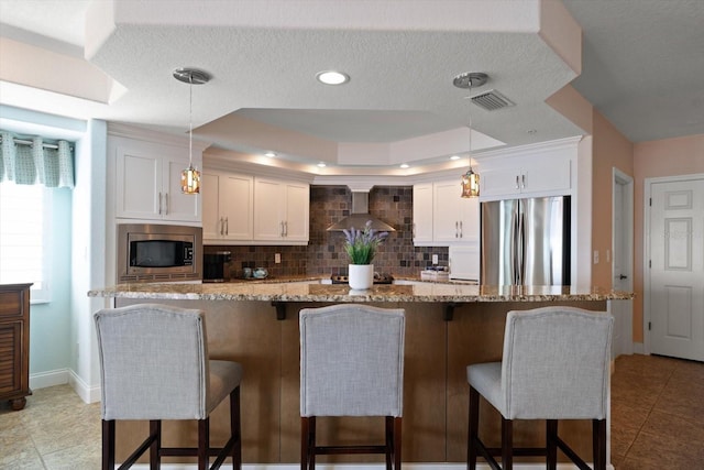 kitchen featuring wall chimney exhaust hood, a kitchen bar, appliances with stainless steel finishes, and white cabinets