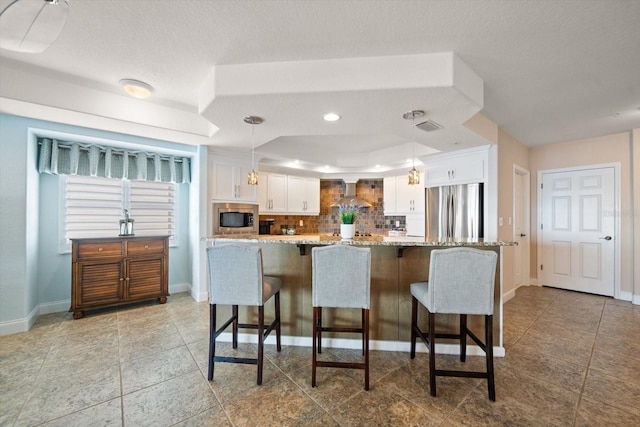 kitchen with a breakfast bar, decorative light fixtures, stainless steel appliances, a raised ceiling, and white cabinets