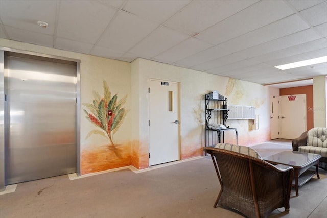 living area with elevator, a drop ceiling, and concrete floors