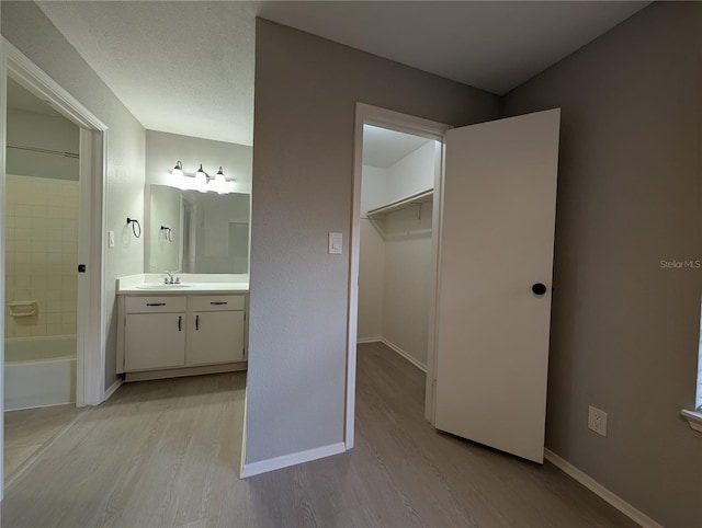 bathroom featuring baseboards, bathtub / shower combination, wood finished floors, and vanity