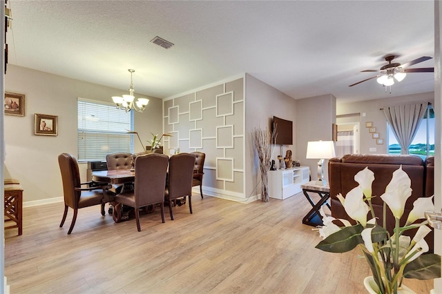 dining area with light wood finished floors, visible vents, a textured ceiling, baseboards, and ceiling fan with notable chandelier