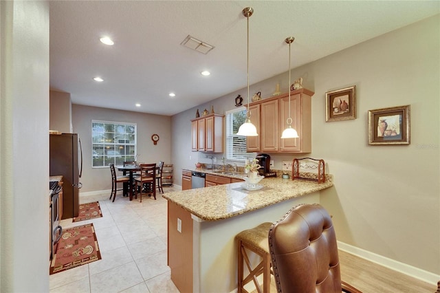 kitchen with appliances with stainless steel finishes, light stone counters, a kitchen breakfast bar, a peninsula, and pendant lighting