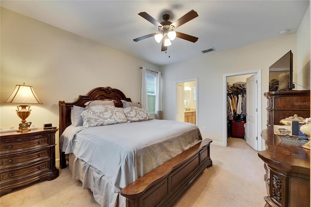 bedroom featuring ceiling fan, ensuite bathroom, light carpet, visible vents, and a walk in closet