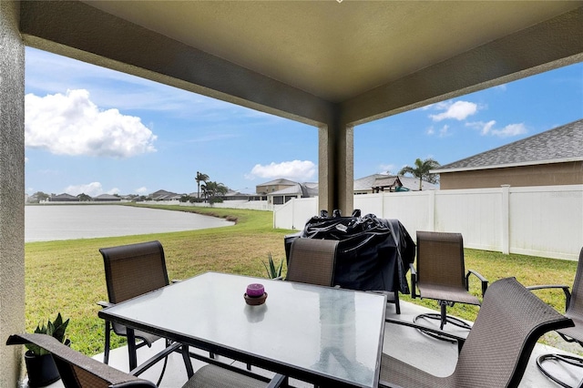 view of patio featuring a water view, a grill, fence, and outdoor dining area