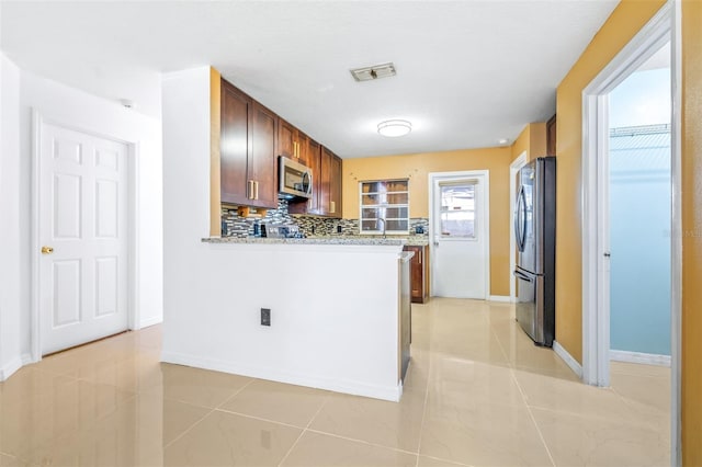 kitchen with visible vents, decorative backsplash, appliances with stainless steel finishes, brown cabinetry, and baseboards