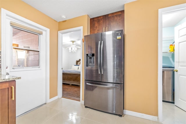 kitchen featuring light tile patterned flooring, stainless steel fridge, baseboards, and light stone countertops