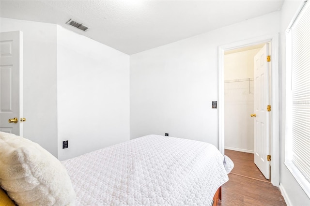 bedroom featuring a closet, visible vents, a spacious closet, a textured ceiling, and wood finished floors