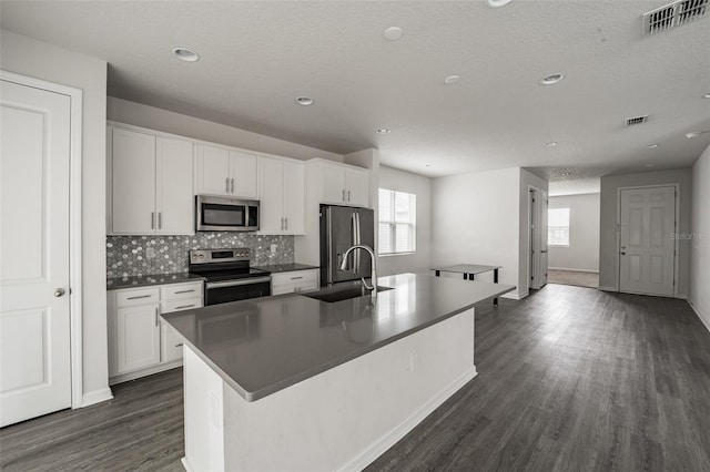 kitchen featuring appliances with stainless steel finishes, dark countertops, a center island with sink, and white cabinets