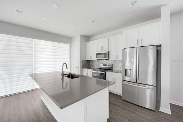 kitchen with a center island with sink, dark countertops, stainless steel appliances, white cabinetry, and a sink