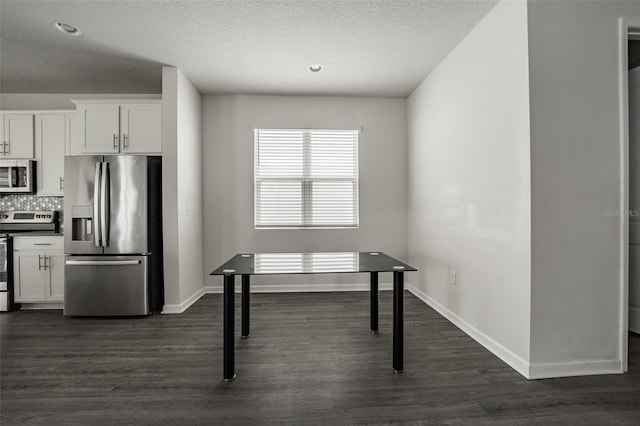 kitchen with white cabinets, dark countertops, appliances with stainless steel finishes, dark wood-type flooring, and backsplash