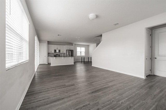 unfurnished living room with dark wood-style flooring, visible vents, and baseboards