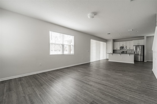 unfurnished living room featuring baseboards, dark wood finished floors, and a textured ceiling