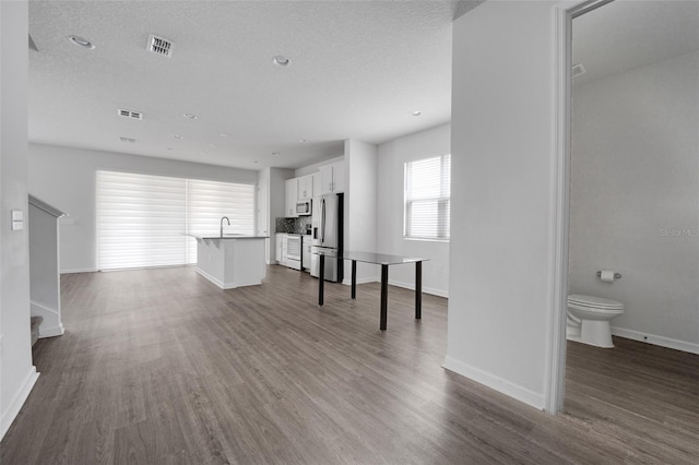 unfurnished living room with dark wood finished floors, visible vents, a sink, a textured ceiling, and baseboards