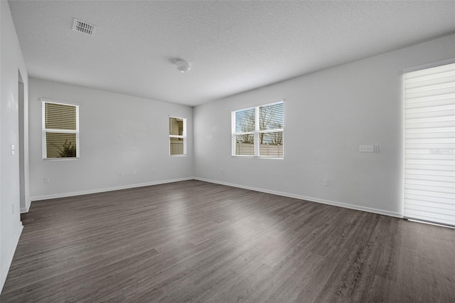 empty room featuring baseboards, a textured ceiling, visible vents, and dark wood-style flooring