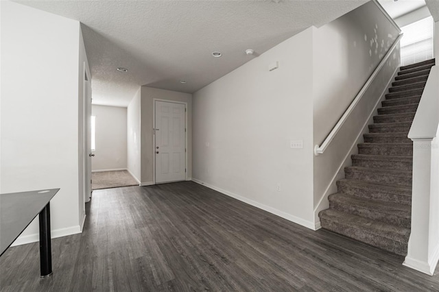 entrance foyer with a textured ceiling, stairway, dark wood-style flooring, and baseboards