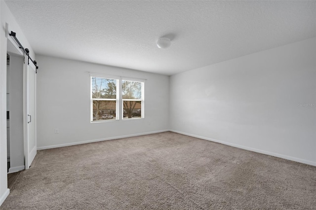 unfurnished bedroom with carpet floors, a barn door, and baseboards