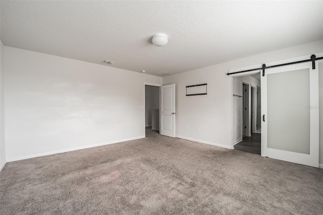 empty room with a barn door, baseboards, dark colored carpet, and a textured ceiling