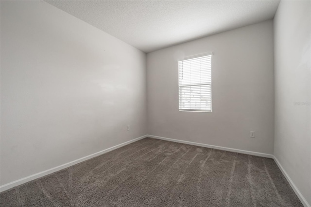 empty room featuring a textured ceiling, dark carpet, and baseboards