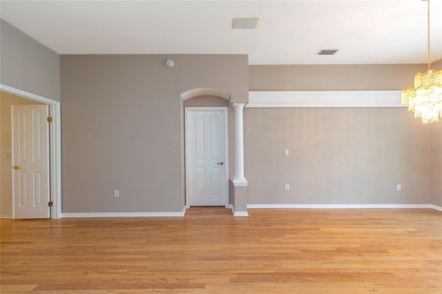 spare room with visible vents, light wood-style flooring, decorative columns, baseboards, and a chandelier