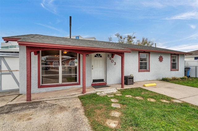 view of front facade featuring a shingled roof, a front yard, fence, and stucco siding