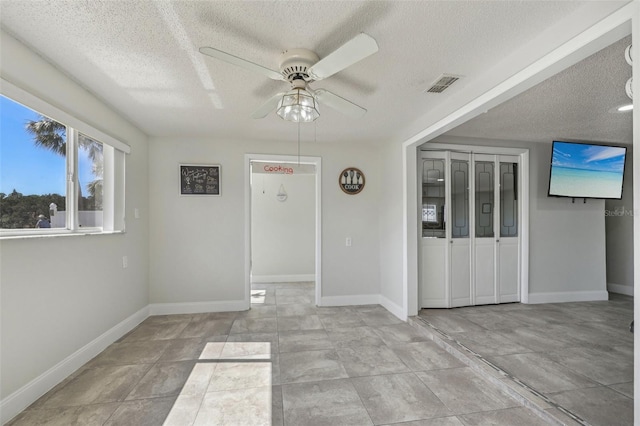 empty room featuring baseboards, a textured ceiling, visible vents, and a ceiling fan