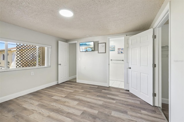 unfurnished bedroom featuring light wood-type flooring, baseboards, and a textured ceiling