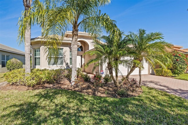 view of front of home featuring a garage, a tiled roof, decorative driveway, stucco siding, and a front lawn