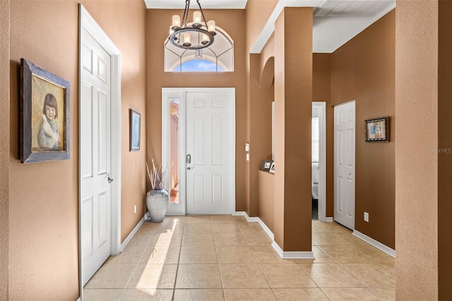 entrance foyer with baseboards, a high ceiling, light tile patterned flooring, and an inviting chandelier