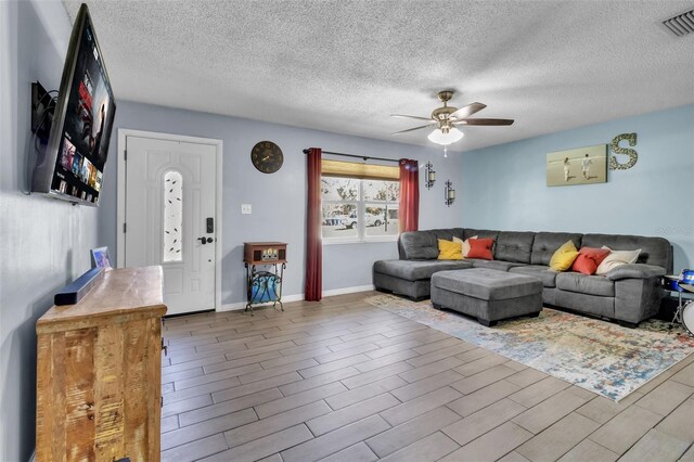 living area featuring visible vents, a textured ceiling, wood finished floors, and a ceiling fan