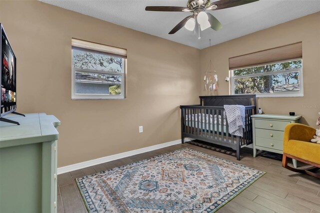 bedroom with a nursery area, baseboards, and wood finished floors