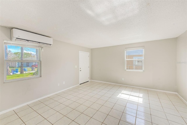 spare room featuring light tile patterned floors, a textured ceiling, a wall mounted air conditioner, and baseboards