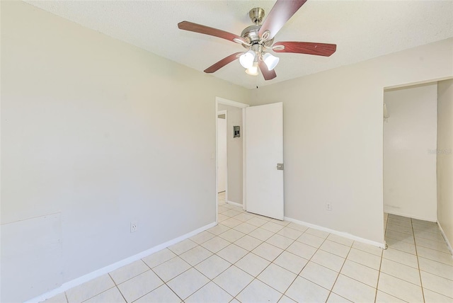 empty room with light tile patterned floors, ceiling fan, baseboards, and a textured ceiling