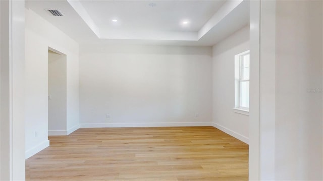 unfurnished room featuring visible vents, light wood-style flooring, baseboards, and a tray ceiling