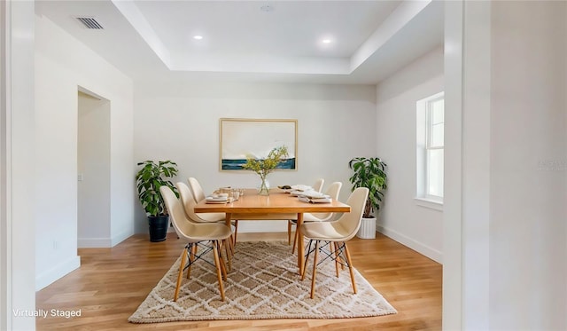 dining space with a tray ceiling, light wood-type flooring, baseboards, and visible vents