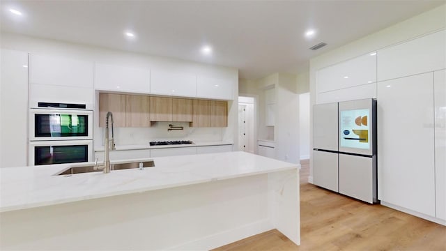 kitchen featuring a sink, white appliances, modern cabinets, and light wood finished floors