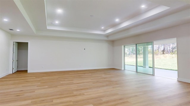 empty room with baseboards, visible vents, light wood-style flooring, recessed lighting, and a raised ceiling