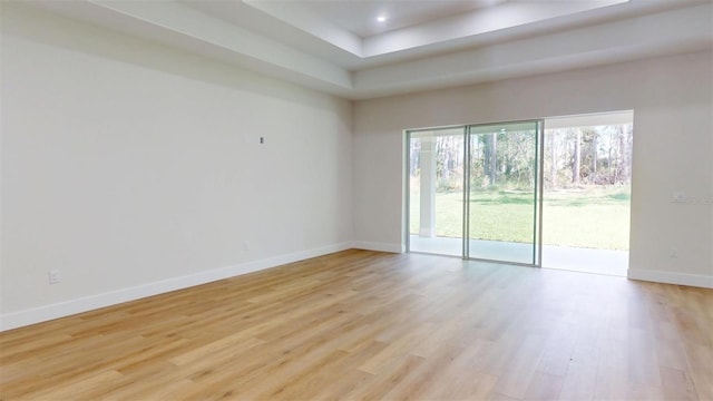 unfurnished room with recessed lighting, a tray ceiling, light wood-type flooring, and baseboards