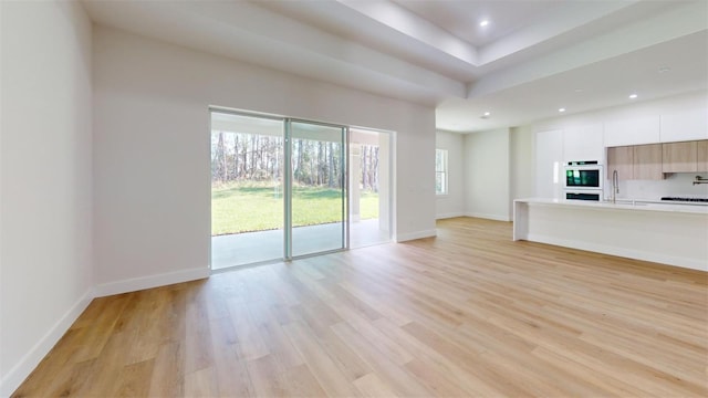 unfurnished living room featuring recessed lighting, light wood-style floors, baseboards, and a sink