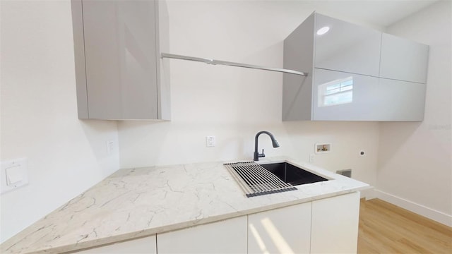 kitchen featuring modern cabinets, light wood-style flooring, light stone countertops, and a sink