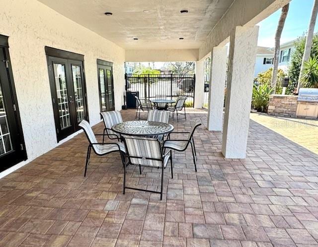 view of patio with outdoor dining area, french doors, a grill, fence, and exterior kitchen