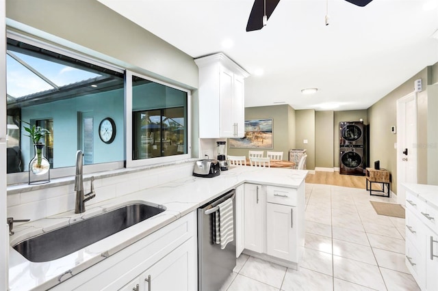 kitchen featuring dishwasher, stacked washing maching and dryer, a sink, and white cabinetry