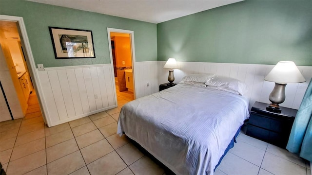 bedroom with a wainscoted wall, ensuite bathroom, and light tile patterned flooring