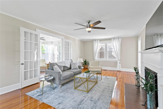 living area featuring ceiling fan, wood finished floors, a fireplace with flush hearth, and baseboards