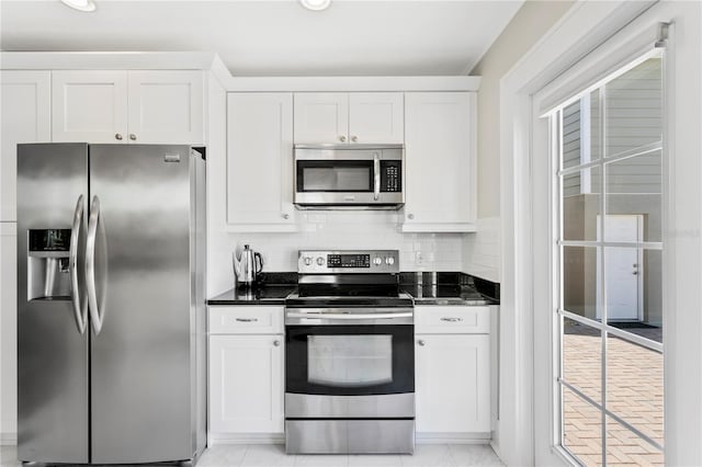 kitchen with stainless steel appliances, tasteful backsplash, dark stone countertops, and white cabinets