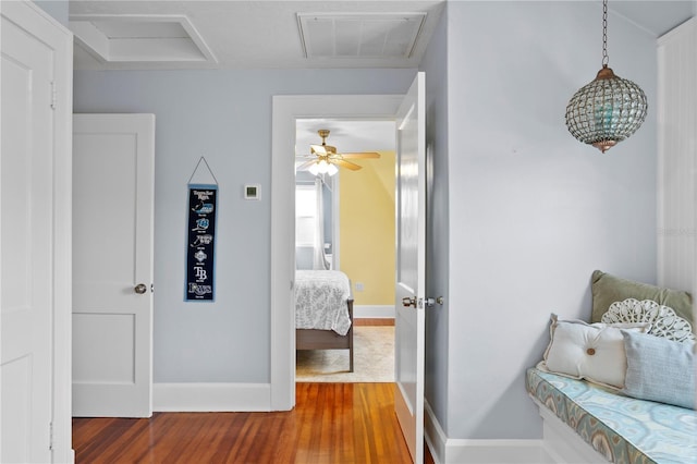 hall with attic access, visible vents, baseboards, and wood finished floors