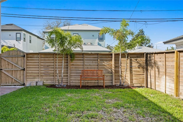 view of yard featuring a balcony, a fenced backyard, and a gate